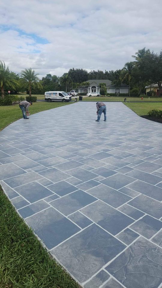A tool with a long blue handle is being used to smooth and level freshly laid concrete on a sidewalk. The surface is wet and shiny, with visible demarcation lines separating the individual concrete slabs. Naples Concrete Solutions excels in providing top-notch resurfacing and concrete repair services for any project.