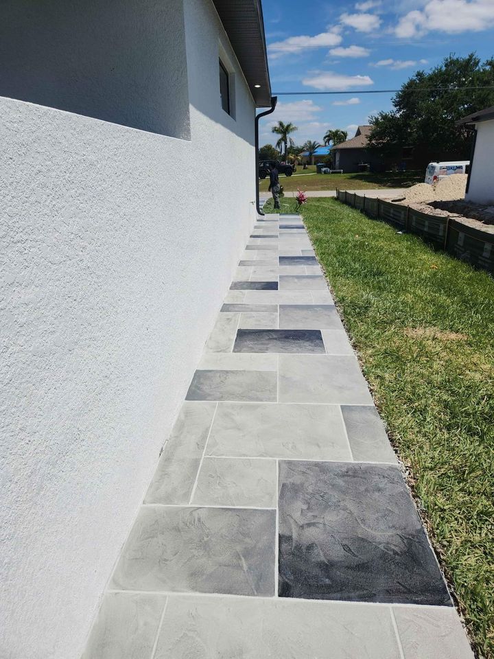 A construction worker from Naples Concrete Solutions uses a long-handled concrete broom to smooth and texture a fresh concrete sidewalk. The area is surrounded by dirt and partially completed wooden forms outline the path, ensuring quality in every step of resurfacing the pavement.