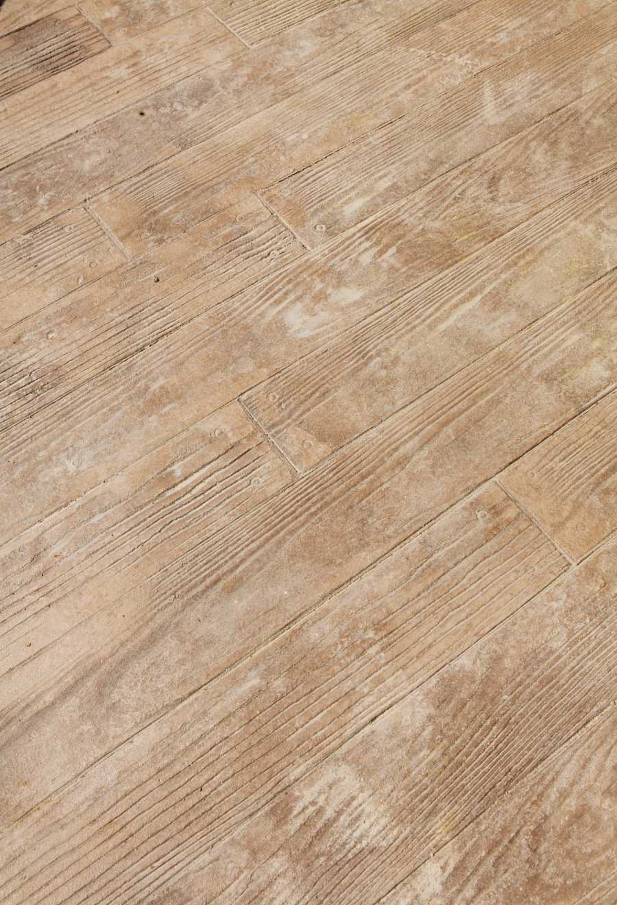 A close-up view of a weathered wooden floor with natural tan and light brown hues. The floorboards have visible grain and texture, giving it a rustic appearance reminiscent of a stamped concrete patio in Naples FL.